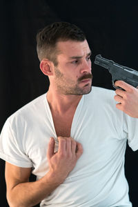 Man attempting suicide with gun against black background