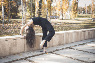 Side view of woman stretching at park during autumn