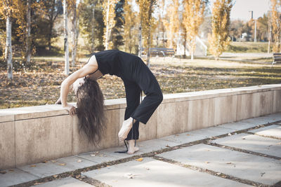 Full length of young woman with arms raised against trees