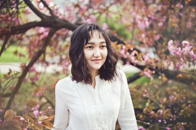 Young attractive asian woman in a white shirt under the blooming sakura tree in park, calm, smiling