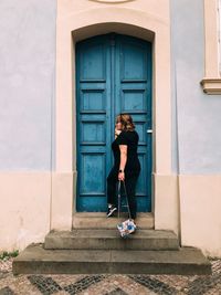 Full length of woman standing against door of building