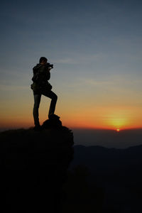 Silhouette man photographing on mountain against sky during sunset