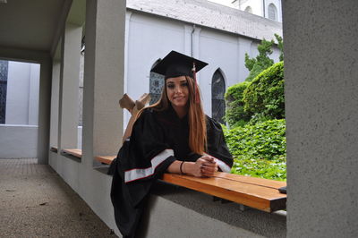 Portrait of smiling female graduate lying down on bench in university