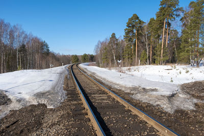 Railroad tracks amidst trees against clear sky during winter