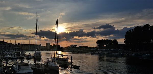 Sailboats moored at harbor against sky during sunset