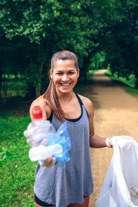 Portrait of woman holding garbage while standing on footpath against trees