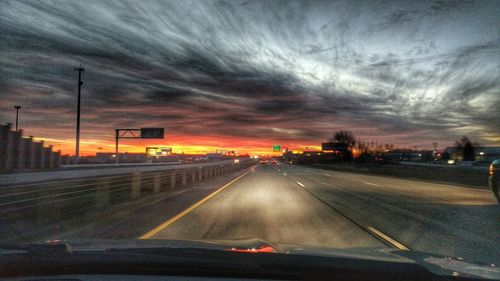 Cars on road against cloudy sky at sunset