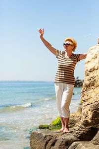 Elderly attractive smiling woman standing on a rock on the seashore