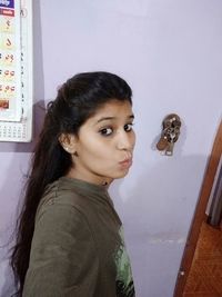 Portrait of young woman standing against wall at home