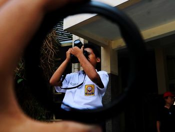 Cropped hand holding lens against male friend photographing with camera