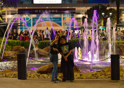 Rear view of people standing against illuminated lights at night