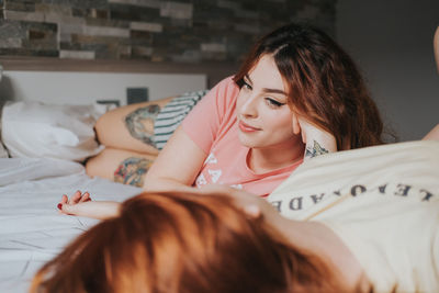 Crop young female girlfriends in pajamas relaxing on bed in bedroom