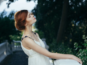 Side view of young woman against trees