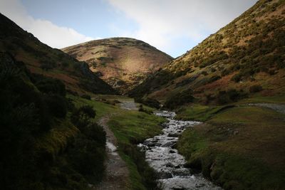 Scenic view of stream amidst mountains against sky