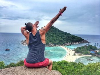 Rear view of man gesturing on cliff against sea