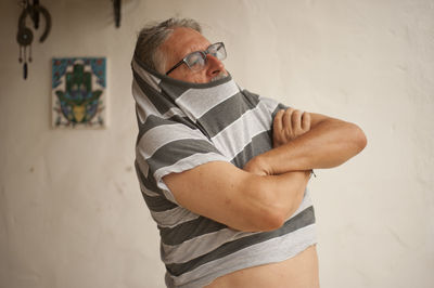 Senior man removing striped t-shirt at home
