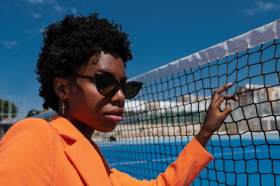 Young african american woman with short hair and sunglasses, dressed in a stylish orange outfit