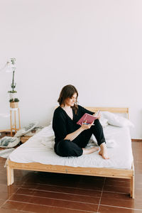 Young woman sitting on book against wall