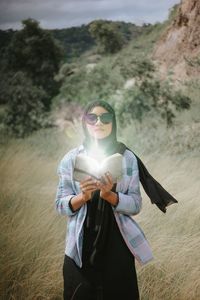 Portrait of young woman wearing sunglasses standing on field