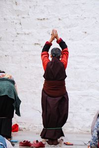 Rear view of a monk praying against wall