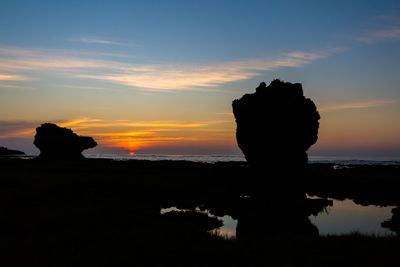 Silhouette rock on sea against sky during sunset