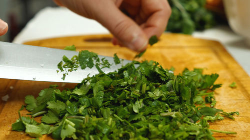 A cook cuts parsley with a sharp knife on a kitchen board. side view. vegetarian kitchen