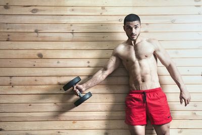 Shirtless man exercising against wooden wall