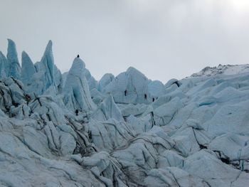 Distance shot of unrecognizable climbers ice climbing on jagged glacial seracs with a gray sky