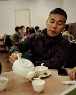 Mature man pouring drink in cup while sitting at cafe