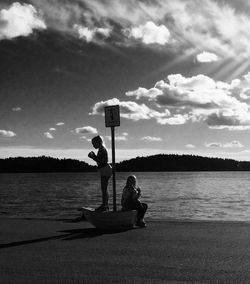 Silhouette people on calm lake in front of mountain range