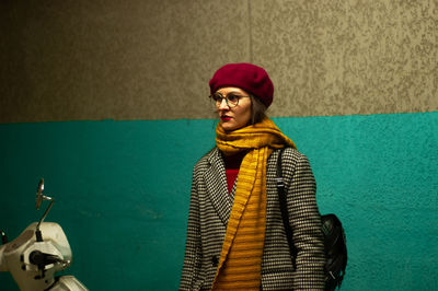 Young woman in warm clothes standing against wall