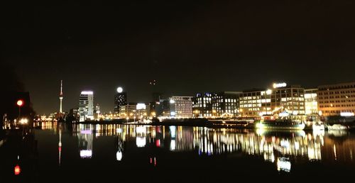 Illuminated buildings by river against sky at night