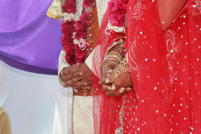 Midsection of bride and groom with hands clasped during ceremony