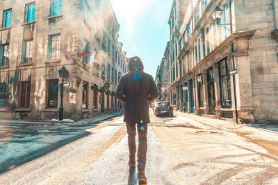 Rear view of man walking on street amidst buildings