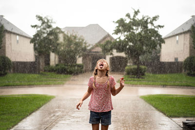 Playful girl with mouth open standing on driveway during rainfall