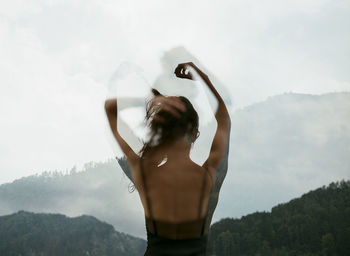 Midsection of woman with arms raised standing on mountain against sky