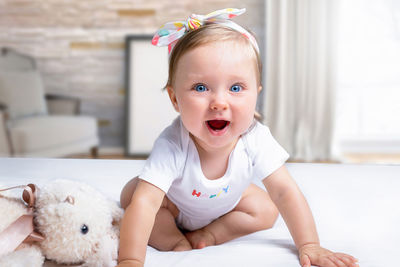 Portrait of cute baby girl sitting on bed at home