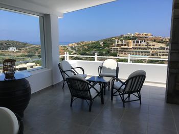 Chairs and table in balcony by sea against sky