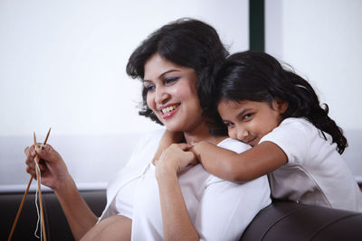 Happy daughter embracing pregnant mother sitting at home