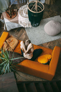 An overhead view of a woman sitting on a sofa in her home in a lotus position 