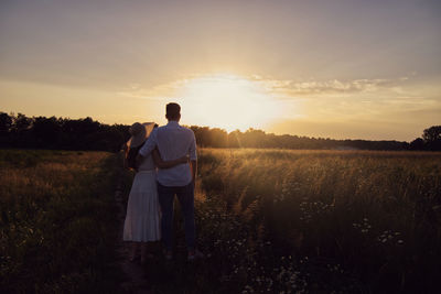 Rear view of man standing on field against sky during sunset