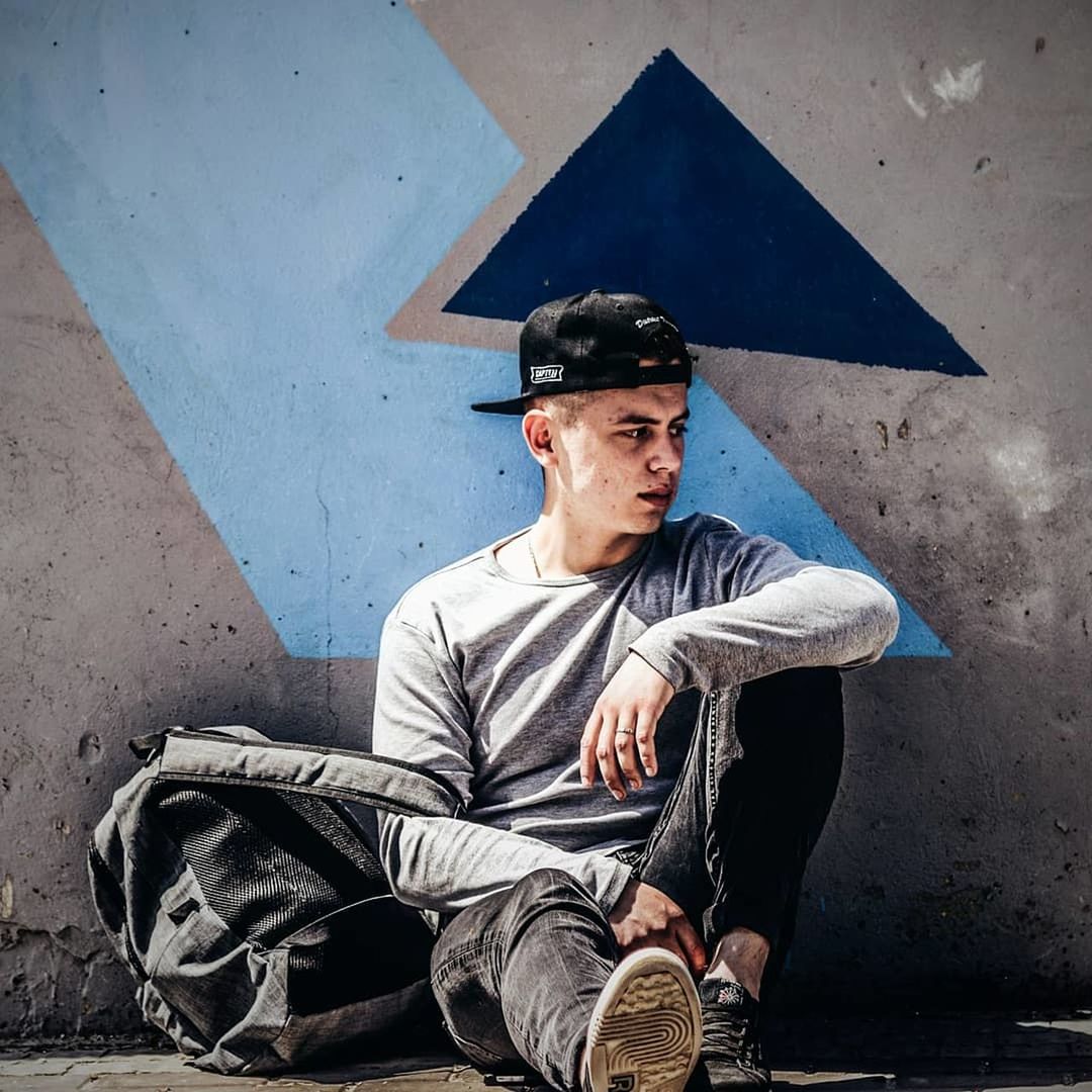 one person, real people, lifestyles, wall - building feature, front view, young adult, young men, sitting, leisure activity, casual clothing, full length, looking away, day, looking, architecture, three quarter length, men, contemplation, fashion, outdoors