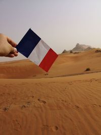 Person holding umbrella on desert against sky