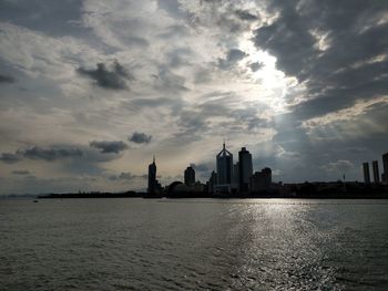 City at waterfront against cloudy sky