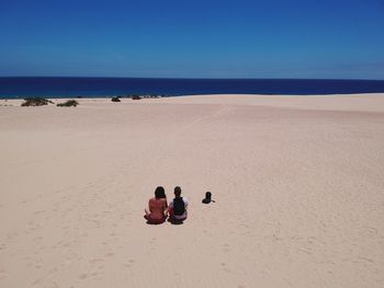 High angle view of couple sitting on beach against clear sky