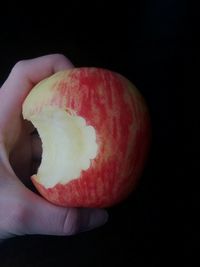 Close-up of hand holding apple against black background