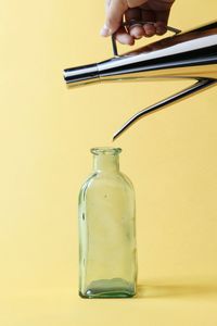 Cropped hand feeling glass jar against yellow background