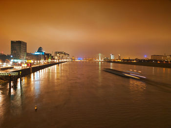 Illuminated buildings by river against sky at night