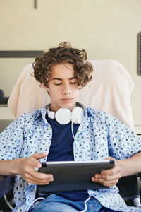 Teenage boy watching movie on digital tablet while sitting against van