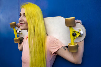 Portrait of young woman holding yellow while standing against blue wall